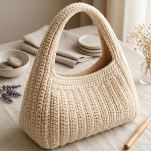Könnte beinhalten: Eine beige gehäkelte Handtasche mit einem dicken, strukturierten Rippenmuster und einem einzelnen integrierten Henkel. Die Tasche ist in einer dichten Maschentechnik gefertigt, was eine strukturierte, abgerundete Form mit einer weiten Öffnung ergibt.