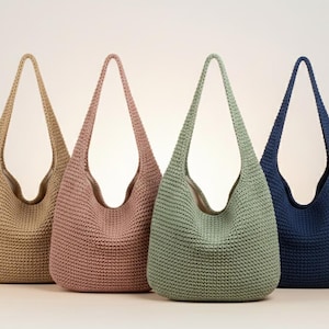 Op de afbeelding: Vier schoudertassen in hobo-stijl gemaakt van een getextureerde, gehaakte gebreide stof. De tassen staan op een rij en hebben vier verschillende effen kleuren: beige, oudroze, saliegroen en marineblauw. Elke tas heeft een geïntegreerde schouderband.