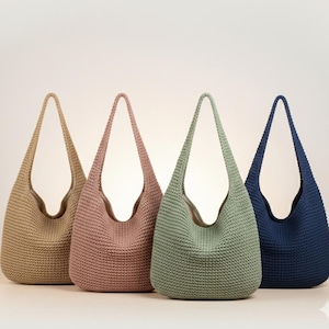 May include: Four crochet tote bags in a row, each with a long handle. The bags are in shades of tan, pink, green, and navy blue. The bags have a rounded bottom and a wide opening.