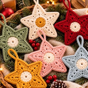 May include: A set of five crocheted star ornaments in cream, red, sage green, light pink, and mustard yellow. Each star features a contrasting circular center and a small loop at the top for hanging, arranged together in a woven basket.