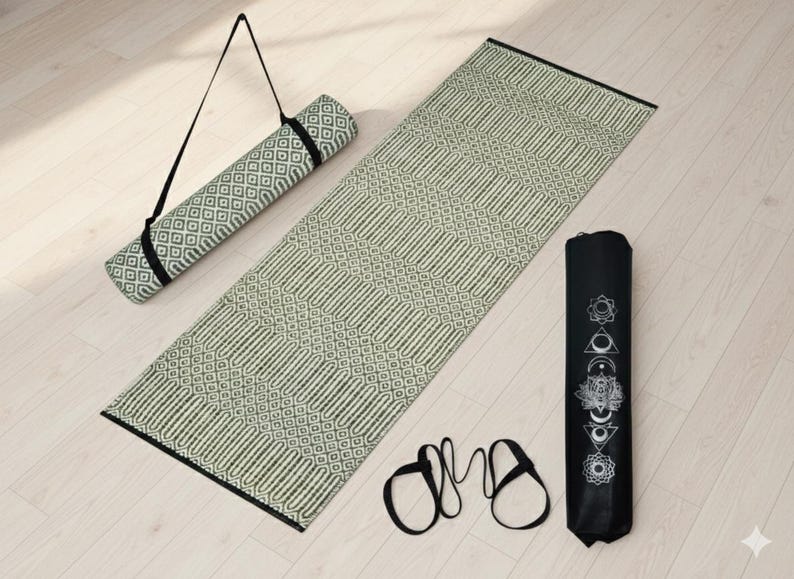 Puede incluir: Una esterilla de yoga rectangular con un patr&oacute;n geom&eacute;trico repetitivo en blanco roto y verde oscuro. Se incluye una esterilla de yoga enrollada a juego con una correa negra, una bolsa cil&iacute;ndrica negra con s&iacute;mbolos de chakras blancos y una correa.