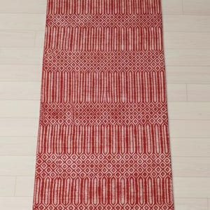 Puede incluir: Una alfombra de pasillo rectangular con un vibrante patr&oacute;n geom&eacute;trico en rojo y blanco. El dise&ntilde;o consiste en bandas horizontales alternas de formas de diamante intrincadas y motivos verticales alargados, creando una textura sim&eacute;trica.