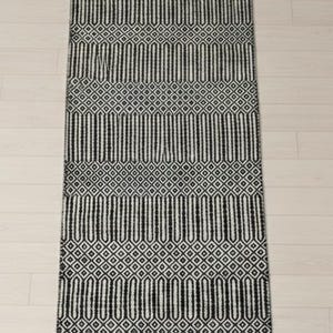 Puede incluir: Una alfombra de pasillo rectangular con un patr&oacute;n geom&eacute;trico repetitivo en blanco y negro. El dise&ntilde;o consta de bandas horizontales alternas de formas ovaladas verticales alargadas y peque&ntilde;as cuadr&iacute;culas de rombos, con un borde negro s&oacute;lido.