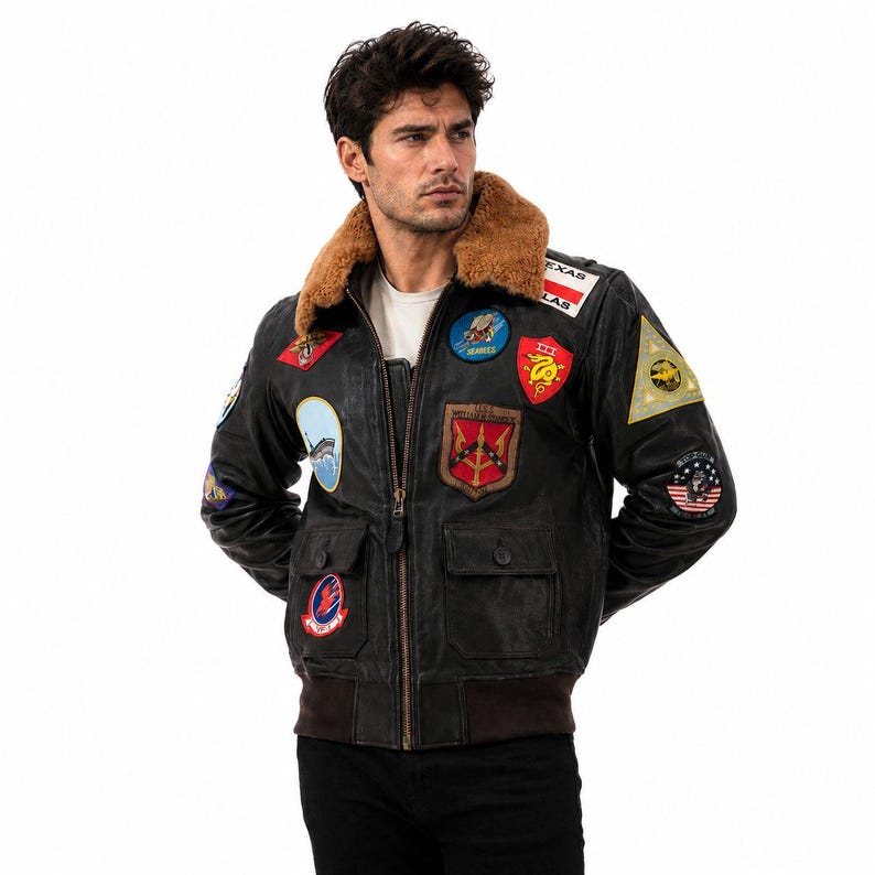 Peut inclure: Un blouson aviateur en cuir noir avec un col en fausse fourrure marron, une fermeture &eacute;clair frontale et deux poches &agrave; rabat. La veste est orn&eacute;e de divers &eacute;cussons brod&eacute;s color&eacute;s sur la poitrine et les manches, incluant du texte et des motifs.
