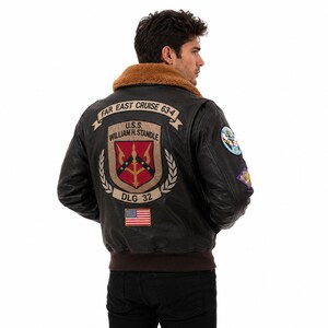 Peut inclure: Un blouson aviateur en cuir marron fonc&eacute; avec un col en fausse fourrure beige et un ourlet c&ocirc;tel&eacute; marron. Le dos pr&eacute;sente des &eacute;cussons brod&eacute;s avec le texte FAR EAST CRUISE 63-4, U.S.S. WILLIAM H. STANDLE, DLG 32 et un drapeau des &Eacute;tats-Unis.