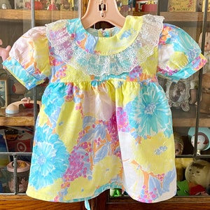 May include: A yellow, blue, and pink floral print dress with a white lace collar. The dress has short sleeves and a gathered skirt.