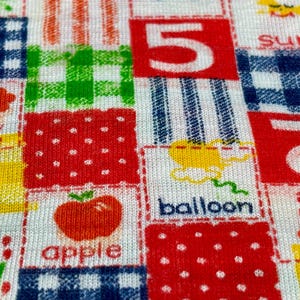 May include: A colorful fabric with a patchwork design featuring various words and numbers. The words include "sun", "tree", "apple", and "balloon". The numbers include "5" and "2".