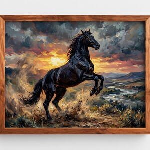 May include: A framed wall art print featuring an oil painting of a black horse rearing up on a hillside. The background displays a dramatic sunset with dark clouds, a winding river, and distant mountains. The frame is made of medium-toned wood.