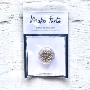 May include: A small clear plastic container filled with gold and silver crown jewels gems. The container is labeled "Maker Forte Crown Jewels Gems High-quality gems to add sparkle to your projects www.Makerfortecom".