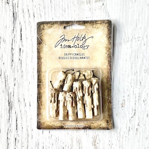 May include: A pack of nine miniature off-white drippy candles by Tim Holtz idea-ology. The rectangular cardboard backing features a distressed, aged appearance with the text "Tim Holtz idea-ology" and "Drippy Candles" printed on the front.