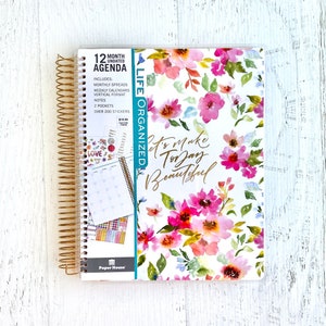 May include: A floral-patterned 12-month undated agenda with gold wire-o binding. The cover features a watercolor floral design with pink, blue, and green flowers. The text "Let's make today beautiful" is printed in gold on the cover.