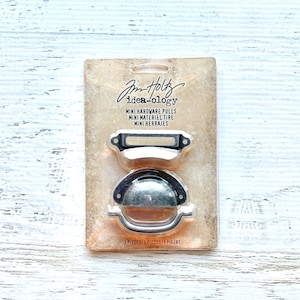 Könnte beinhalten: Eine Packung mit drei silberfarbenen Mini-Hardware-Griffen, beschriftet mit "Jim Holtz idea-ology MINI HARDWARE PULLS MINI MATÉRIEL TIRE MINI HERRAJES 3 PIECES/3 PIECES/3 PIEZAS".