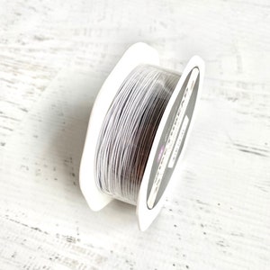 May include: A spool of white elastic cord, wound around a white plastic bobbin. The bobbin has a black label with white text.