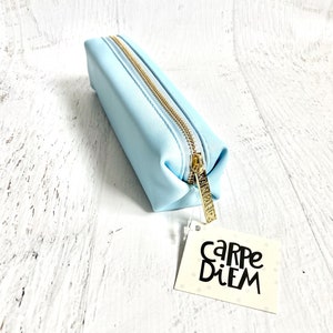 May include: A light blue pencil case with a gold zipper and a tag that says "Carpe Diem".