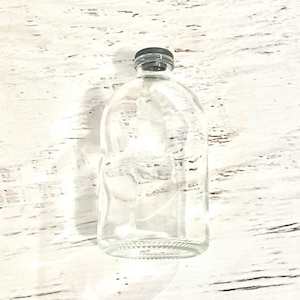 May include: A clear glass bottle with a black lid. The bottle is empty and has a textured surface.