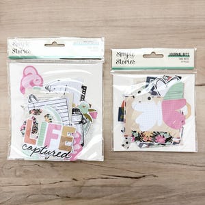 May include: Two packages of Simple Stories ephemera. One package has the text "LIFE captured" and the other says "JOURNAL BITS". The ephemera includes paper cutouts with floral and geometric designs, and other decorative elements.