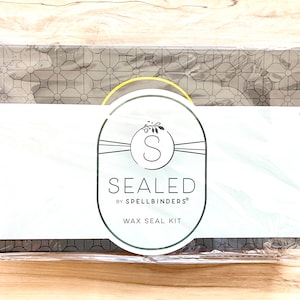 Peut inclure: Un kit de sceau de cire scellé par Spellbinders. Le kit est emballé dans une boîte rectangulaire avec un motif floral gris. Il comprend une étiquette blanche avec les mots "SEALED" et "WAX SEAL KIT".