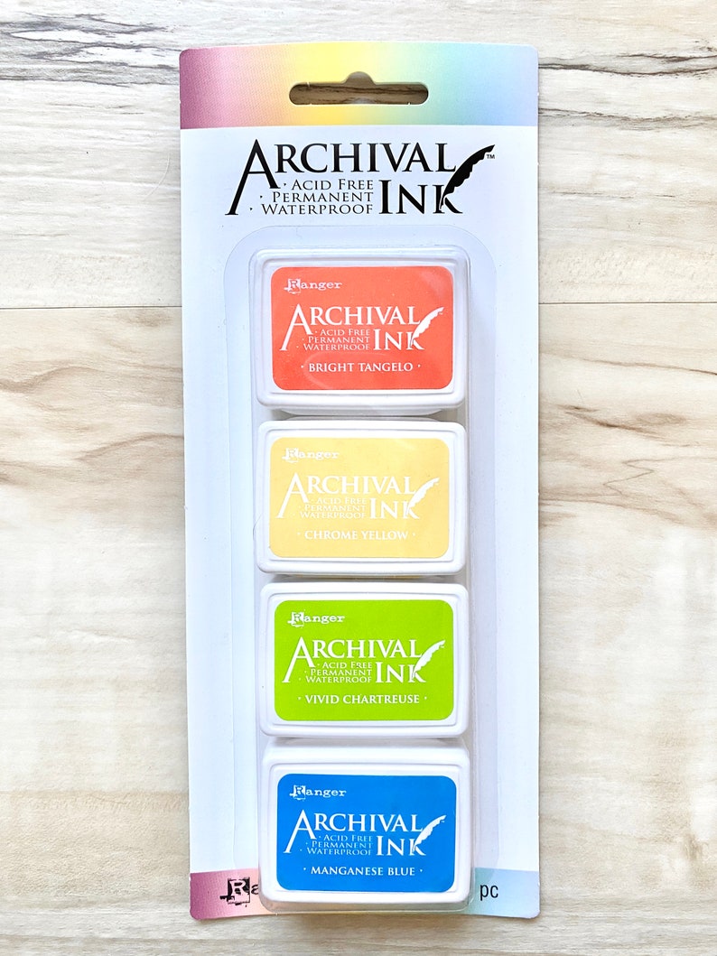 May include: Four ink pads in a clear plastic packaging. The ink pads are labeled "Ranger Archival Ink" and are in the colors bright tangelo, chrome yellow, vivid chartreuse, and manganese blue.