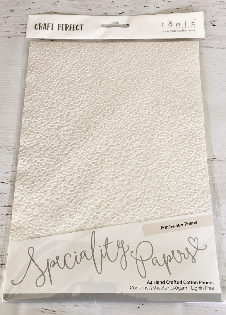 May include: A pack of 5 sheets of Freshwater Pearls A4 hand crafted cotton paper. The paper is white with a textured surface that resembles small pearls. The pack is labeled "Speciality Papers" and "Craft Perfect".
