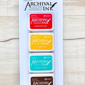 May include: A set of four archival ink pads in a clear plastic packaging. The ink pads are labeled with the colors Carnation Red, Sunflower, Garden Patina, and Potting Soil. The ink pads are acid-free, permanent, and waterproof.