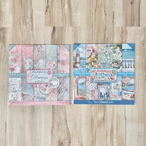 May include: Two packages of scrapbook paper featuring a blue and white nautical theme and a pink and blue floral theme. The packages each contain 10 double-sided sheets of paper. The text on the packages reads "Stamperia Dream Scrapbooking" and "Stamperia Blue Dream Scrapbooking".