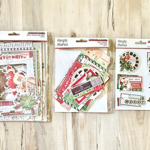 May include: Three packages of Christmas themed paper crafting supplies from Simple Stories. The first package contains a variety of frames, papers, and embellishments. The second package contains a variety of die-cut shapes and stickers. The third package contains a variety of stickers and embellishments.