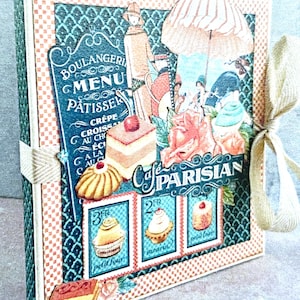 Kit de álbum interactivo DIY Cafe Parisian de Graphic 45, con instrucciones, papel, cinta, adornos y posibilidad de crear tarjetas con las piezas sobrantes.