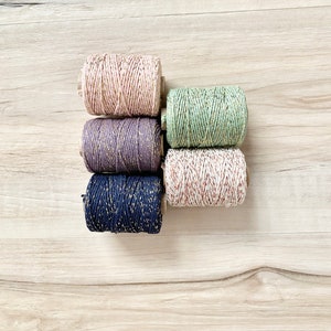 May include: Five spools of twine with gold glitter. The spools are in the colors pink, green, purple, navy blue, and beige.