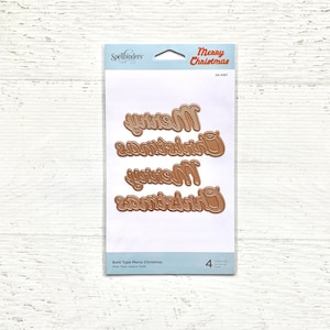 Könnte beinhalten: Eine Packung Spellbinders-Stanzformen zum Basteln. Die Packung ist weiß mit einer blauen Kopfzeile und dem Text "Merry Christmas" in Rot. Die Stanzformen sind golden und buchstabieren "Merry Christmas".
