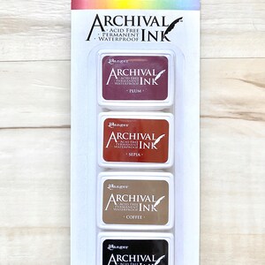 May include: A set of four ink pads in a clear plastic packaging. The ink pads are labeled "Ranger Archival Ink" and are in the colors plum, sepia, coffee, and jet black. The ink pads are acid free, permanent, and waterproof.