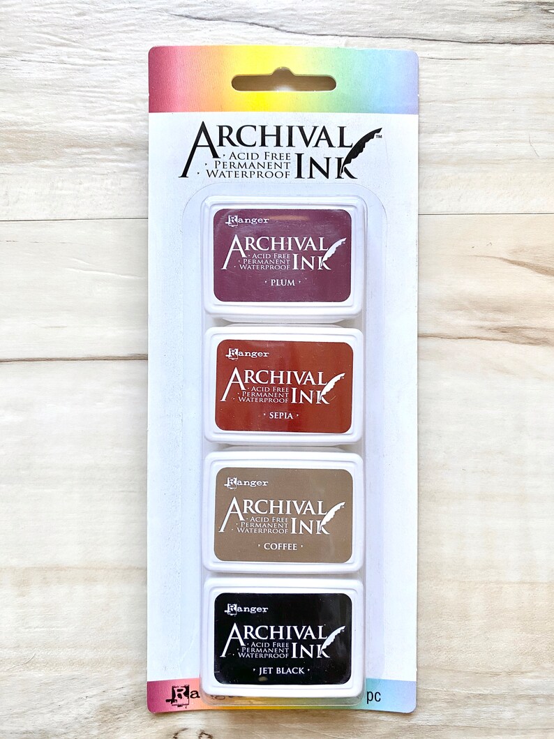May include: A set of four ink pads in a clear plastic packaging. The ink pads are labeled "Ranger Archival Ink" and are in the colors plum, sepia, coffee, and jet black. The ink pads are acid free, permanent, and waterproof.