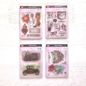 May include: Four clear plastic packages containing clear silicone stamps with various designs. The designs include a Christmas ornament, a boot, a train, a car, a rose, a pocket, a paintbrush, and a bouquet of flowers. The packages are labeled "Silikon-Stempel" and "My Paper World".