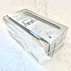 Puede incluir: Una caja de almacenamiento de metal plateado con una tapa de plástico transparente. La caja está etiquetada como "Distress Ink Storage" y tiene una lista de características: "Utilizar para guardar las almohadillas de tinta Distress Oxide de tamaño completo", "Contiene 15 almohadillas de tinta de 2 x 2 pulgadas", "Almacenamiento conveniente y portátil".