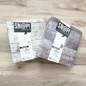 May include: Two 6x8 SN@P! binders by Simple Stories. The left binder features a white wood grain pattern labeled Aspen, while the right binder has a dark brown wood grain pattern labeled Cedar. Both include a black and white product label.