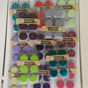 May include: Assortment of colorful bottle caps in various patterns, including zebra print, checkered, and solid colors. The caps are packaged in clear plastic containers with labels that read "Bottle Caps".