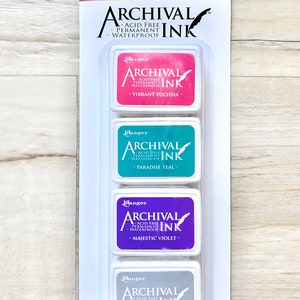 May include: A set of four ink pads in a clear plastic packaging. The ink pads are labeled "Ranger Archival Ink" and are in the colors vibrant fuchsia, paradise teal, majestic violet, and shadow grey.
