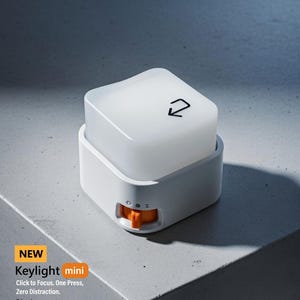 May include: A white Keylight mini with an orange button, designed to focus with one press and zero distraction. The product has a square top with a black arrow symbol. The text "NEW Keylight mini" is visible.