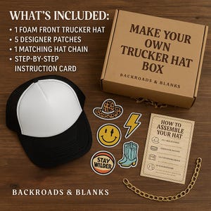 Op de afbeelding: Een zwart-witte trucker-hat kit met een wit voorpaneel, designer patches en een gouden ketting. De kit bevat een doos met de tekst "Make Your Own Trucker Hat Box" en een instructiekaart. De patches bevatten een smiley, bliksemschicht en cowboylaars.