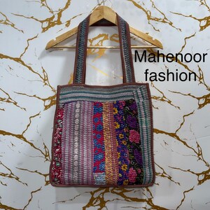 Könnte beinhalten: Eine Patchwork-Tragetasche mit bunten Stoffstreifen und Blumenmustern. Die Tasche hat braune Griffe und Verzierungen, und der Text "Mahenoor fashion" ist auf der rechten Seite sichtbar.