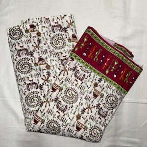 May include: Two folded fabric pieces with a white background and a repeating pattern of figures, houses, and circular designs in red, green, and brown. One piece has a red border with green and yellow figures.
