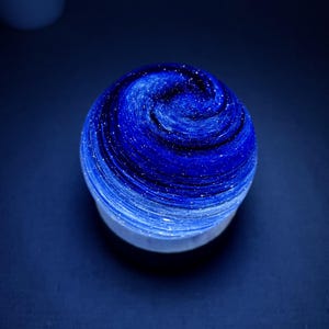May include: A spherical object with a swirling blue and white design, resembling a galaxy or nebula. The object has a white base and a gradient of dark to light blue with white speckles. The overall effect is cosmic and artistic.