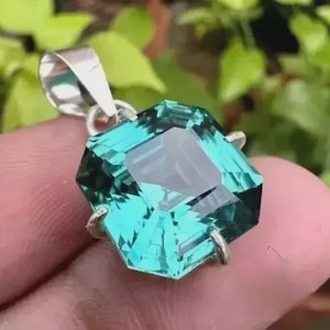 Puede incluir: Colgante de plata con una piedra preciosa facetada de color turquesa. La piedra está tallada en forma geométrica y refleja la luz. Probablemente una pieza de joyería.