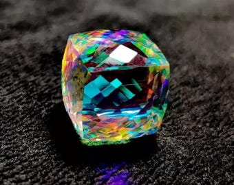 May include: A faceted gemstone with a rainbow of colors, including blue, green, yellow, and red. The gem has a square shape with multiple facets that reflect light. The gemstone is set against a dark, textured background.