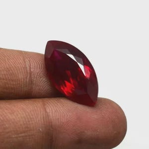 Può includere: Una pietra preziosa taglio marquise di colore rosso intenso e vibrante con una superficie sfaccettata che riflette la luce. La pietra ha una forma ovale allungata e appuntita con lati simmetrici, mostrando una qualità chiara e trasparente.
