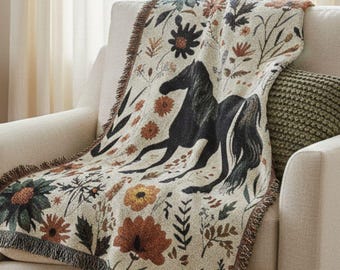 May include: A cream-colored throw blanket with a black horse illustration and floral accents in orange, green, and brown. The blanket is draped over a cream armchair, adding a touch of rustic charm to the room.