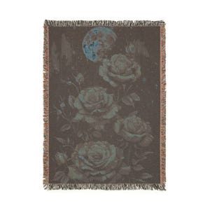 May include: A woven throw blanket featuring a floral design with roses and a full moon. The color palette includes shades of brown, teal, and blue. The blanket has a fringed edge.