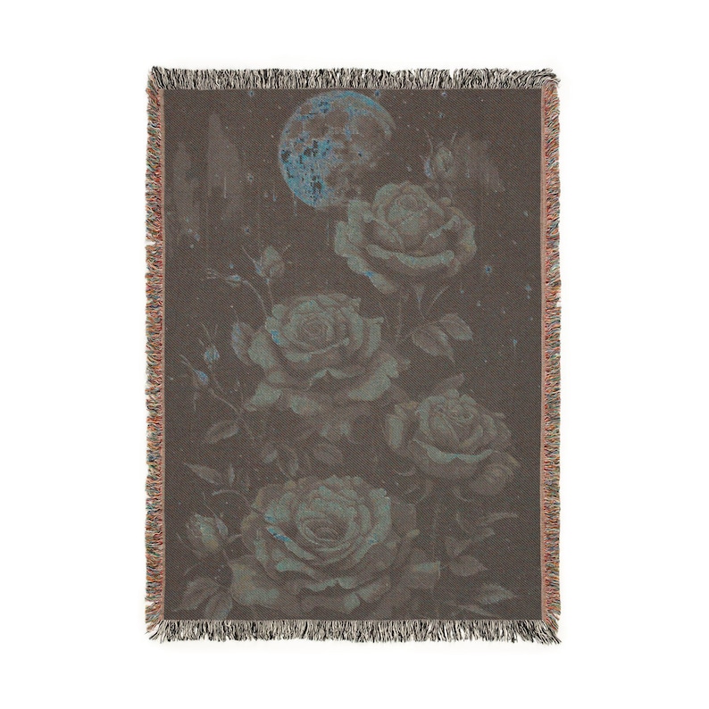 May include: A woven throw blanket featuring a floral design with roses and a full moon. The color palette includes shades of brown, teal, and blue. The blanket has a fringed edge.