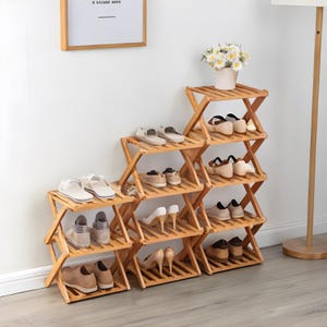 May include: A multi-tiered, foldable wooden shoe rack. The rack is made of light brown wood and features multiple shelves to hold various pairs of shoes. The design is simple and functional, suitable for organizing footwear in a home setting.