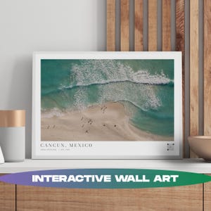 Könnte beinhalten: Ein gerahmter Druck mit einer Strandszene in Cancun, Mexiko. Das Bild zeigt türkisfarbenes Wasser, weiße Wellen und einen Sandstrand mit kleinen Figuren. Der Text "CANCUN, MEXICO" wird unten angezeigt, mit zusätzlichem Text darunter. Die Worte "INTERACTIVE WALL ART" stehen unten.