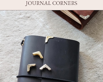 May include: Add-On JOURNAL CORNERS text above a black leather journal secured with a black elastic band. Four metallic corner protectors with embossed scrollwork patterns are placed on the cover. A brown leather journal corner is also visible.